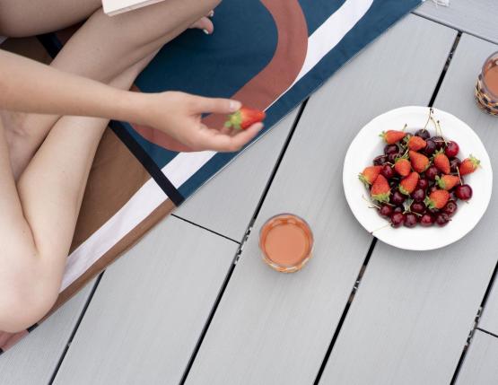 Homme assis en tailleur sur une terrasse en bois composite qui mange des fruits posés dans une assiette