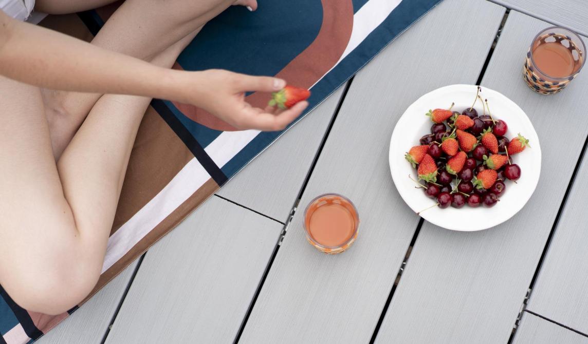 Homme assis en tailleur sur une terrasse en bois composite qui mange des fruits posés dans une assiette