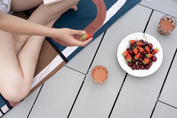 Homme assis en tailleur sur une terrasse en bois composite qui mange des fruits posés dans une assiette
